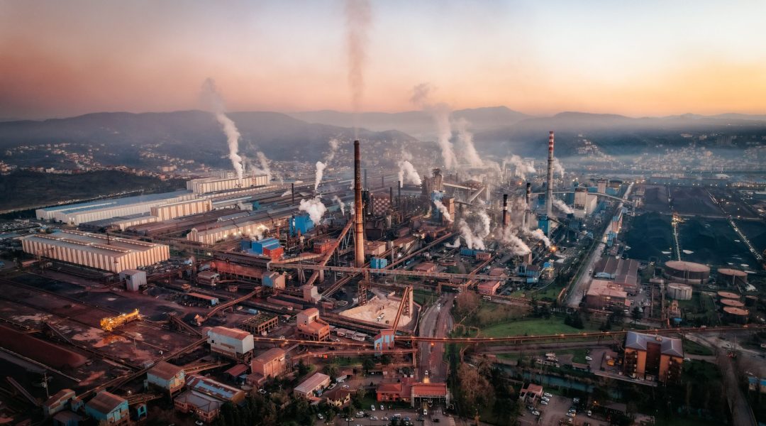 Aerial view of a factory with chimneys emitting smoke during sunset, highlighting industrial pollution.